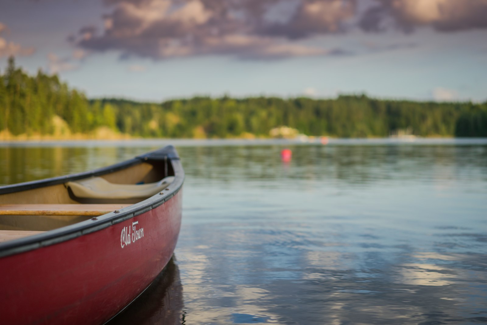 A red canoe floating on a calm lake at a summer camp